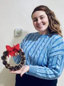 Peer supporter Hannah in blue jumper holding wreath with red bow