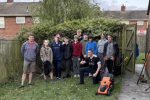 Large group of scouts in a tidy garden, with tools and a lawn mower