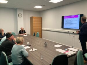 Trustee training session shows 5 people sat at a table while a 6th person is standing presenting,