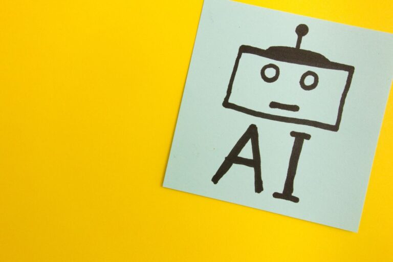 Yellow background with post it note that says AI and has a square robot head.
