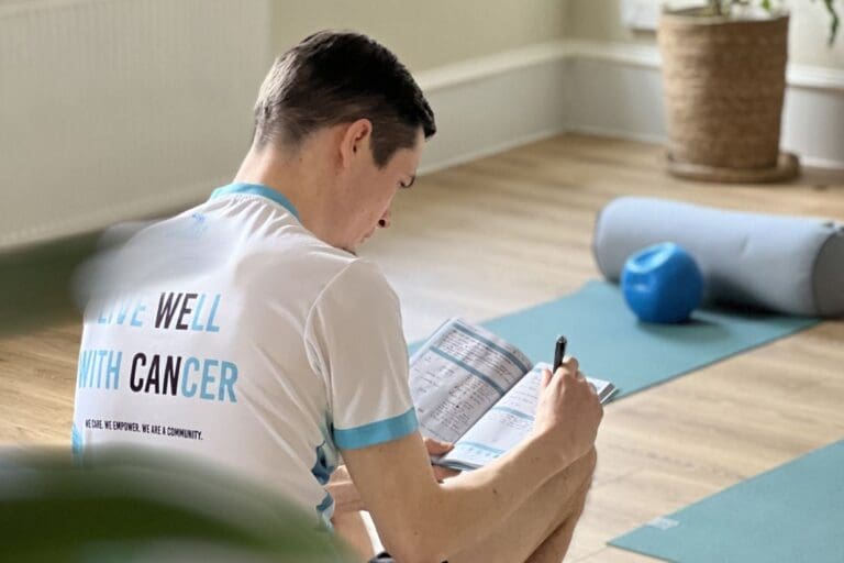 Person with Live Well with Cancer tshirt sat with their back to the camera reading a journal