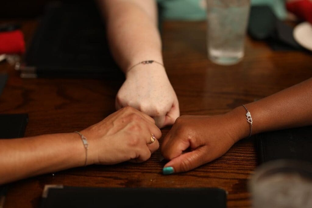 Three hands of different ethnic backgrounds coming together on a table in a fist bump gesture.