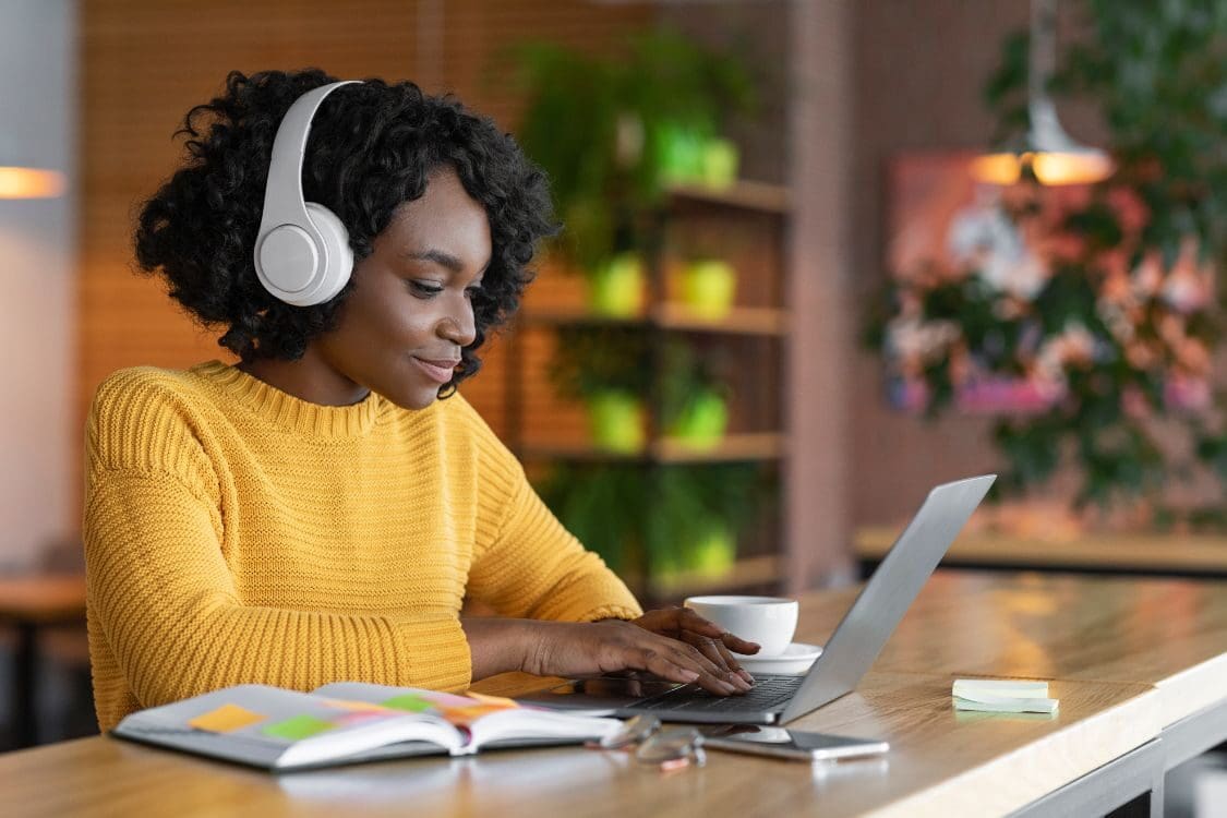 Young woman wearing yellow top having online training, using laptop and wireless headset