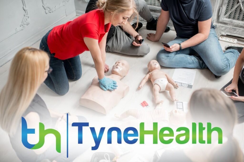 Woman instructor in red top demonstrating how to make chest compressions with a CPR dummy during first aid group training.