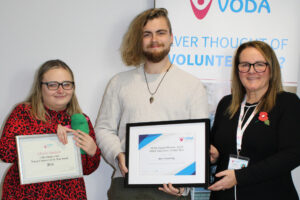 Three people smiling for the camera, two are holding award certificates