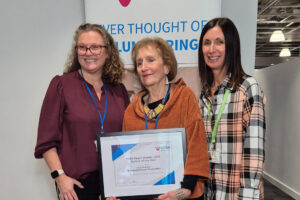Three people smiling for the camera, one person is holding award certificates