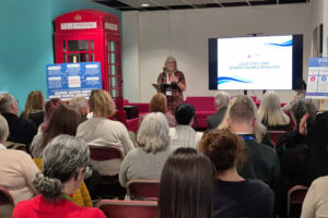 Large group of people sat facing a speaker at the back of the image.
