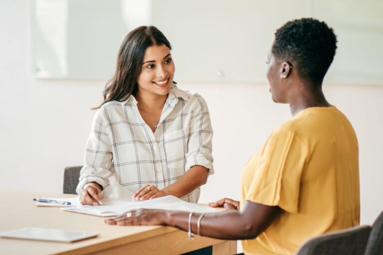 Two women facing each other having a meeting at a light coloured table.