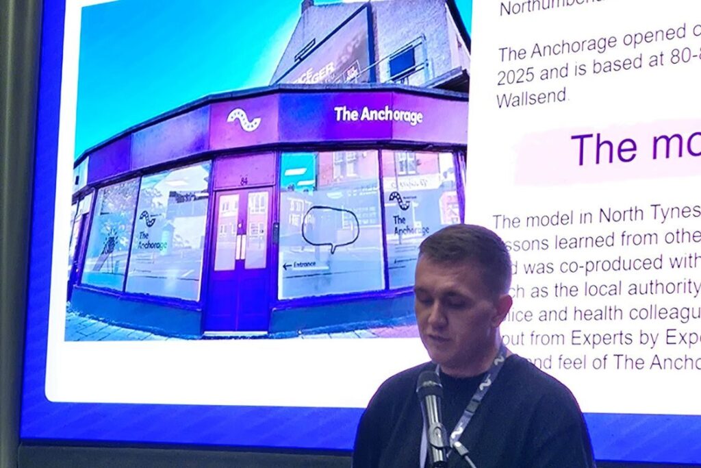 PResenter in front of a screen showing the Safe Haven building behind
