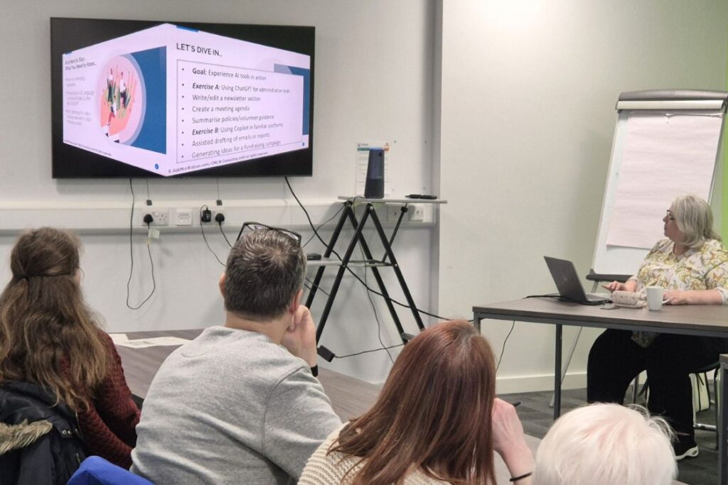 A group of people in a workshop environment facing away from the camera looking at a presentation on screen about AI.