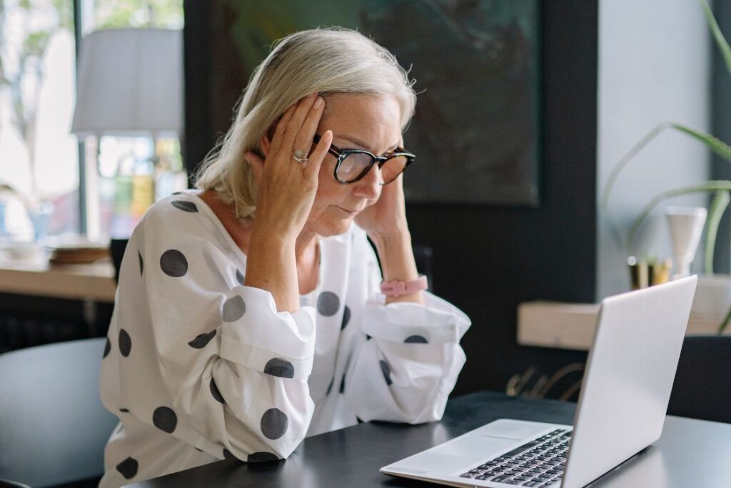 Stressed Woman in white top with black spots, wearing glasses and Using a Laptop