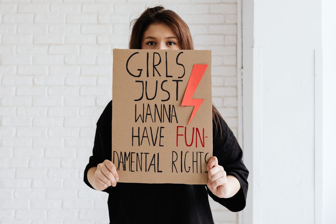 Young woman holding a cardboard sign in front of her which says 'girls just wanna have FUN-deamental rights.