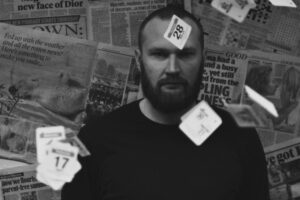 Black-and-white portrait of a person standing in front of a wall covered with newspaper pages, with date cards suspended in the foreground and background as part of the Asylum: A Long and Painful Process photography exhibition.