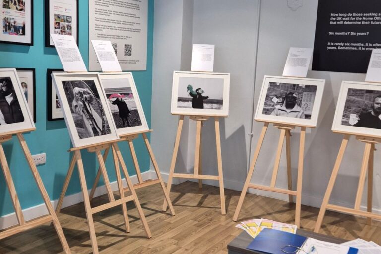 Framed photographs and written testimonies displayed on wooden easels in VODA's reception area as part of Asylum: A Long and Painful Process, an exhibition highlighting the experiences of people seeking sanctuary in the UK.