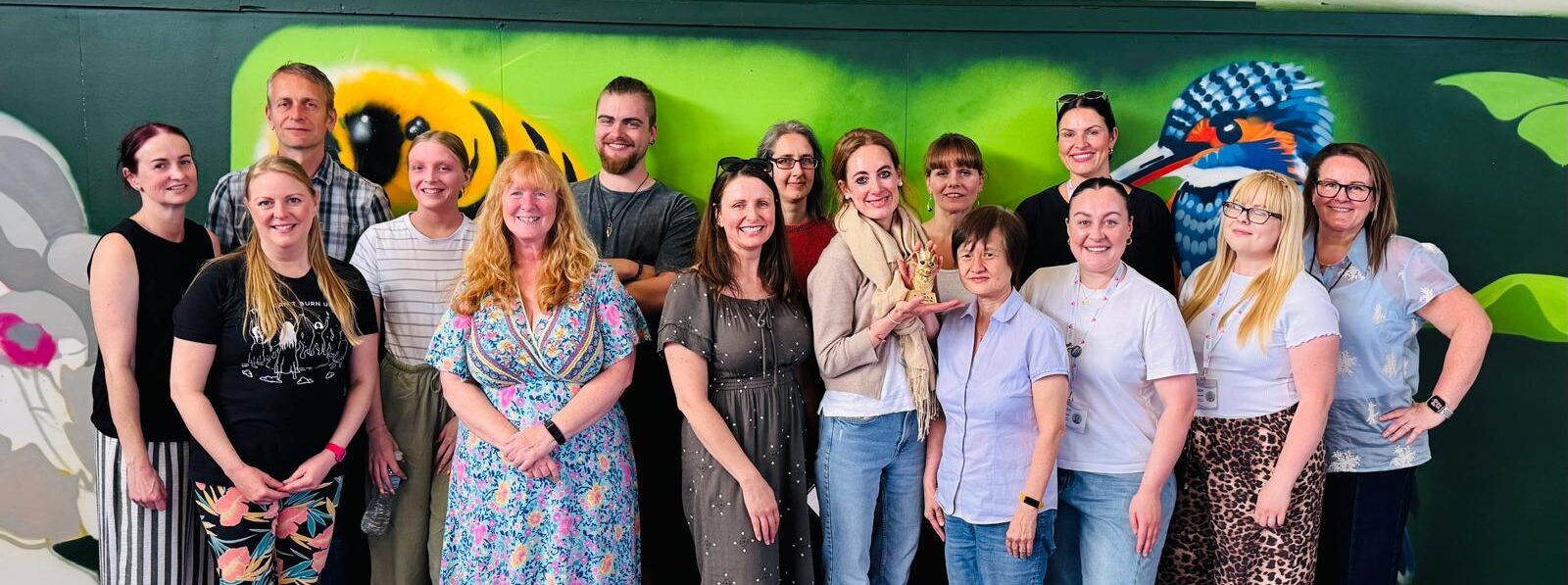A large group of people standing for a group photo in front of a bright green wall