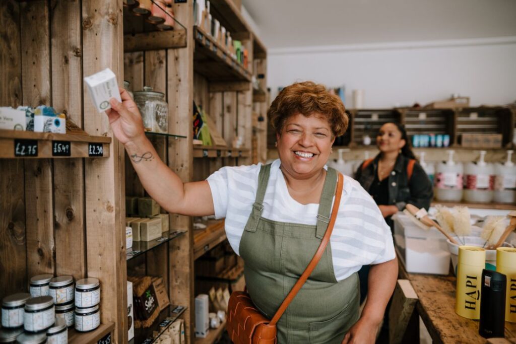 Woman in social supermarket wearing green apron and white top, putting food on a wooden shelf