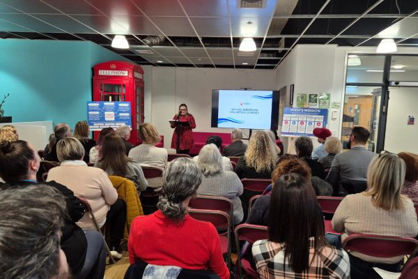 Large group of people sat facing a speaker at the back of the image.